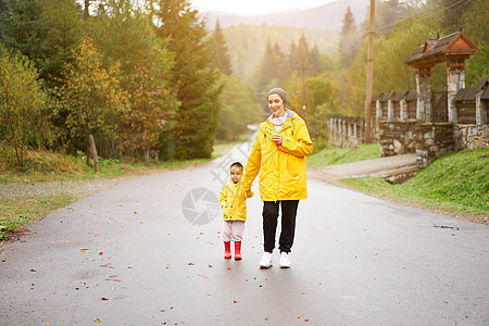 母亲和女儿在雨后行走时穿着黄色雨衣的黄雨衣乐趣幸福妈妈女孩农村生活方式木乃伊下雨闲暇人行道图片