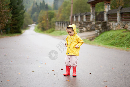玩耍的女孩穿着黄色雨衣 同时在降雨时跳上水坑天气防水乐趣淋浴季节幸福衣服雨滴快乐外套图片