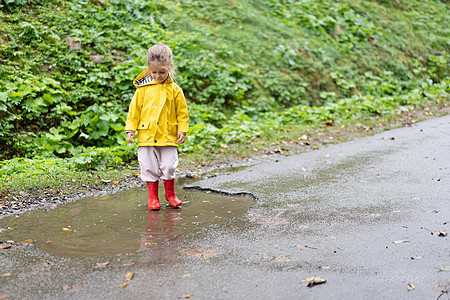 玩耍的女孩穿着黄色雨衣 同时在降雨时跳上水坑乐趣幸福雨滴童年衣服孩子防水天气外套季节图片