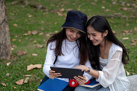 两名女大学生户外学习 在大学公园一起使用数字平板电脑进行校外学习微笑朋友们女士考试知识男人男性技术女性校园图片