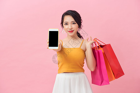 一个相当兴奋的女孩的肖像 带着色彩多彩的购物袋 在粉红背景上显示空白的屏幕手机女士消费者购物狂店铺销售顾客青少年女性图片