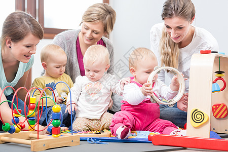 三个快乐的母亲在看婴儿玩着安全的多彩玩具游戏时女性友谊女士托儿所妈妈们母性团体操场父母苗圃图片
