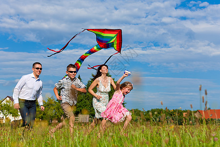 幸福的一家人带着风筝在草地上奔跑微笑蓝色天空快乐孩子们父亲妈妈后代跑步女儿图片
