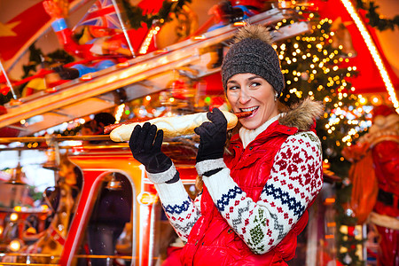女人在圣诞市场吃烤香肠的女士季节旋转木马香肠庆典市场手套包子礼物乐趣图片