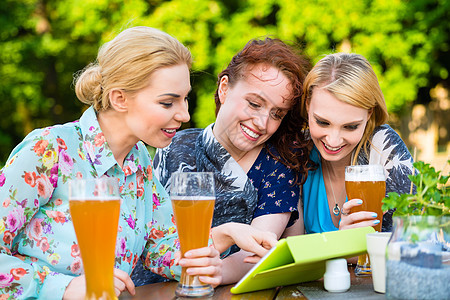 展示朋友在啤酒花园触摸垫子的妇女酒吧眼镜友谊酒精餐厅女性电脑软垫饮料玻璃图片