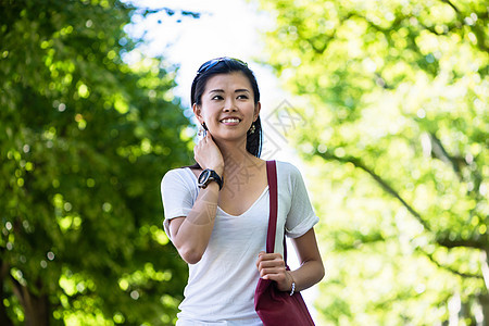 在公园中行走的清廉的年轻女子闲暇叶子娱乐太阳镜游客长发黑发长廊低角度配件背景图片