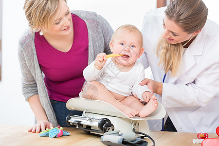 儿科护理专家在衡量女婴体重时微笑 笑容卫生孩子妈妈家庭医生父母医师女性玩具婴儿测量图片