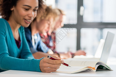 学生在学习时拿笔放在书本上的学生课程桌子女士班级奖学金男性学校微笑知识笔记本图片