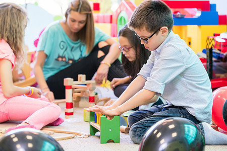 学龄前男孩在幼儿园老师的指导下与孩子们合作团队助手建造女士同事童年教育女孩游戏课堂图片