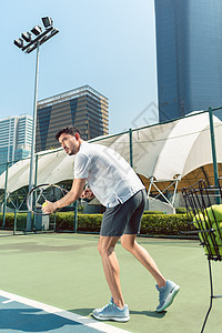 青年男子在城市现代区打网球户外玩网球男性服务摩天大楼玩家场景天空竞赛运动低角度球拍图片