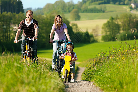 夏季骑自行车的家庭人数锻炼骑术父母头盔树木儿子娱乐男人爸爸晴天图片
