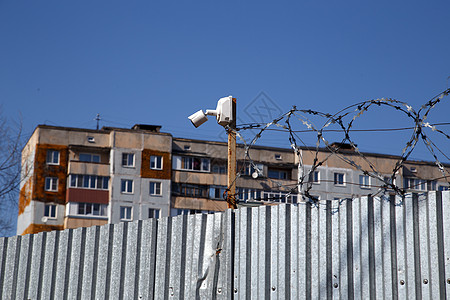 以铁丝网和小型监视摄像头围着围栏的多层住宅楼后防御手表安全相机监控抵押金属建筑民众边界图片