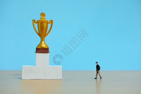 微型商业概念     商务人士在白色讲台上向金奖杯走去男人领导竞赛老板挑战胜利优胜者数字报酬绩效图片