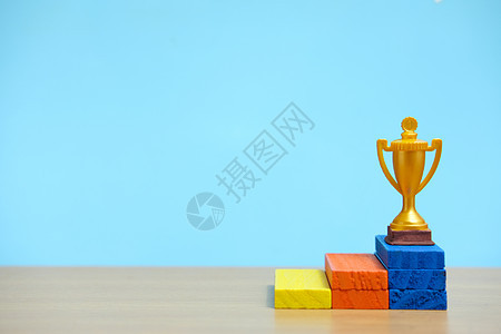 金色奖杯站在木制桌子上五颜六色的领奖台上竞赛运动平台金属报酬勋章比赛胜利锦标赛杯子图片