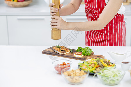 红围裙妇女双手在厨房的切鱼盘上撒散了香料 菜桌上有不同种类的成分和装饰品 在自己家里做饭的幸福感概念背景图片