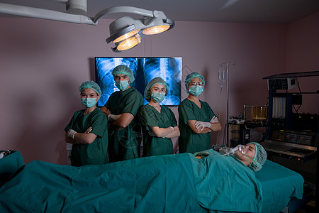 由医生和护士组成的手术团队在手术室里以双臂交叉的自信动作站立 病人躺在床上 医疗保健系统的团队合作支持疾病治疗理念图片