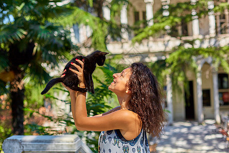 有个年轻女孩在街上跟一只黑小黑猫玩耍闲暇毛皮情感女士动物拥抱微笑猫科朋友友谊图片