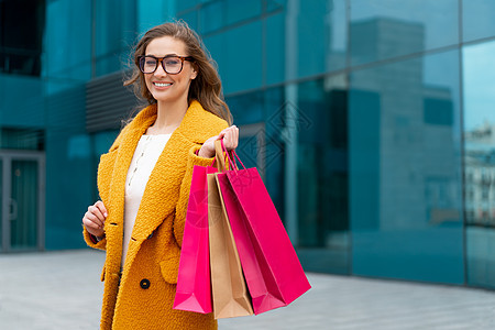 身穿黄大衣 在户外行走的有购物袋的商业妇女公司建筑背景购物中心女性黄色店铺购物外套零售市场微笑女士图片