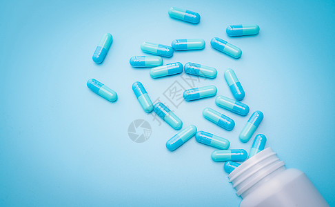 蓝色抗生素胶囊药丸在蓝色背景下从塑料药瓶中散开 抗生素耐药性 抗菌药物滥用 处方药 医药行业 卫生预算背景图片