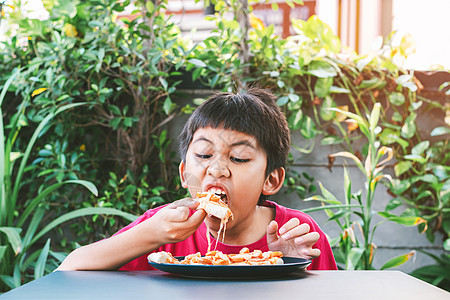 亚洲可爱的男孩 快乐地坐着吃比萨饼沙拉孩子早餐享受小吃桌子午餐食物餐厅孩子们图片