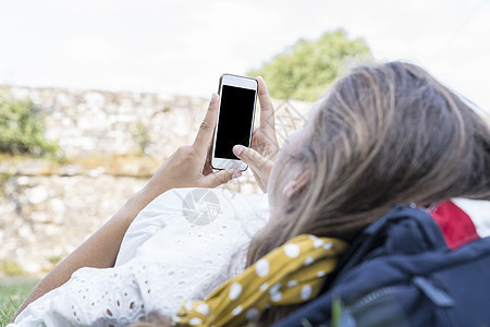 无法辨认的年轻女性手拿着白色手机的模型图像 手里拿着空白的黑色屏幕 同时躺在草地上 在有复制空间的草地上冷藏图片