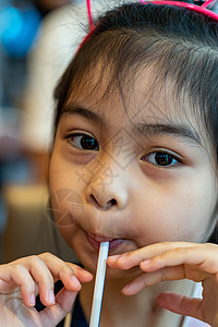 亚洲可爱儿童或小女孩用管子或吸管喝瓶装水或豆奶饮料 吃零食或甜点饮料女性牛奶玻璃黑发稻草果汁营养橙子饮食图片
