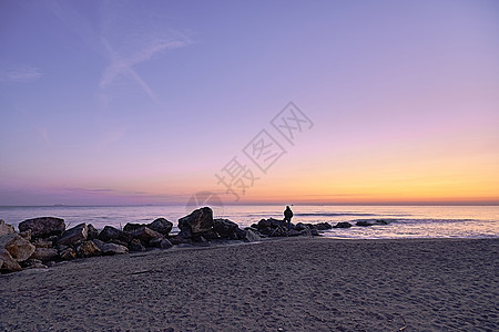 人看日出 从海滩的岩石上海边图片