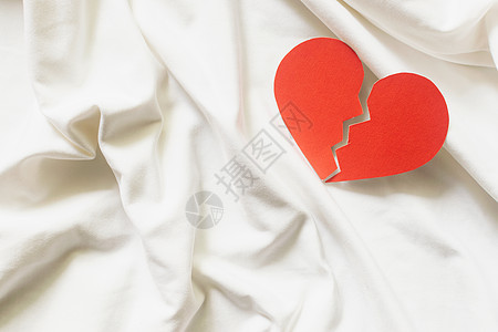 白色纺织品上破碎的红心 离婚概念图片
