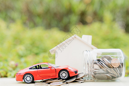 在模糊的绿色自然背景下 一罐硬币和一堆硬币上的红色汽车 存钱和投资概念图片