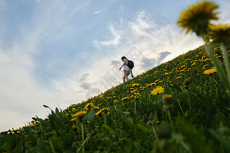 女人在夏日沿着鲜花间道上爬上山坡图片