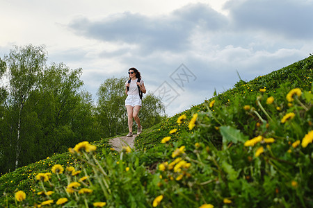 妇女在夏日的花朵中走在一条路上太阳镜风景冒险闲暇背包短裤快乐农村女士活动图片