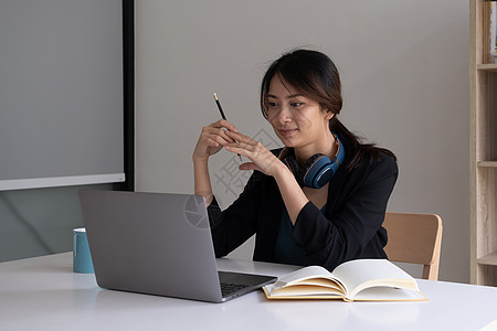 一名妇女穿戴耳机 在笔记本电脑上听教学性网络研讨会图片