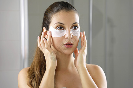 美眉在浴室照镜子时用眼罩遮住脸部 皮肤护理女孩在眼睛下触摸面纱的斑点 以减少眼袋图片