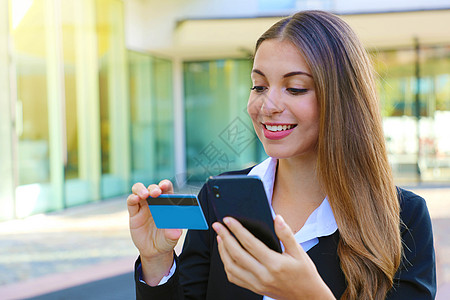 拥有智能手机阅读信用卡号码的女商务人士在休息时间在线上户外办公室购物 人们和网上付款的概念无处不在 (注 )图片
