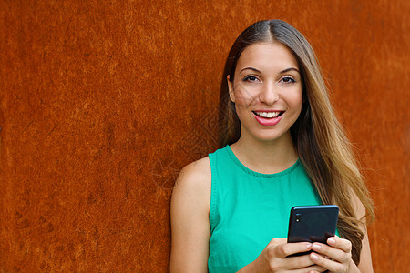 年轻女性使用智能手机 在生锈背景上看相机图片