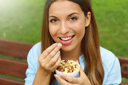 近距离的年轻女子 在公园里吃混合坚果饮食种子水果微笑腰果女士食物花生核桃麦片图片