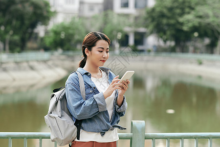 在公园使用智能手机的青年学生技术互联网女孩女性女士电话街道背包快乐城市图片