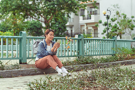 在公园使用智能电话的有吸引力的亚洲女性学生女孩游客视频勘探摄影手机手表背包城市图片