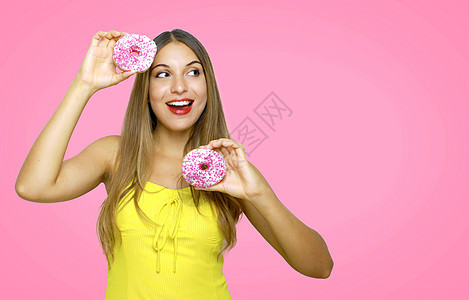 漂亮的有趣的女孩与甜甜圈跳舞 在她的手中 看着侧面的粉色背景 复制空间区域图片