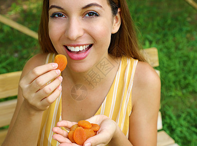 美丽的年轻女子在公园里吃干果 健康的食物概念 (笑声)图片