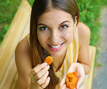 年轻女人在公园里吃干杏子 健康的食物概念图片