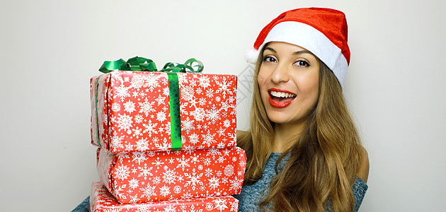 带着白色背景的圣诞节礼物 看着摄影机微笑着年轻的圣诞女人笑容庆典惊喜牙齿展示假期美丽乐趣黑发快乐盒子图片