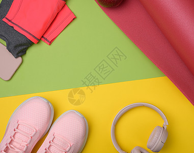 粉色运动鞋 无线耳机 绿色黄色背景的智能手机等红运动垫子工具平铺鞋类褐色活动运动装衣服音乐配件女性图片