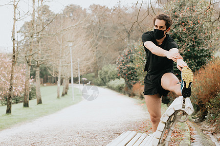 在阳光明媚的一天 一名年轻男性男子在公园长板上拉腿 用面罩复制空间跑步手臂活力训练运动身体慢跑者背痛年轻人男人图片