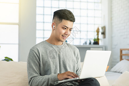 青年男子穿戴耳机 在家用笔记本电脑举行电视会议学习技术工人视频网络房间男人微笑讲话销售量图片