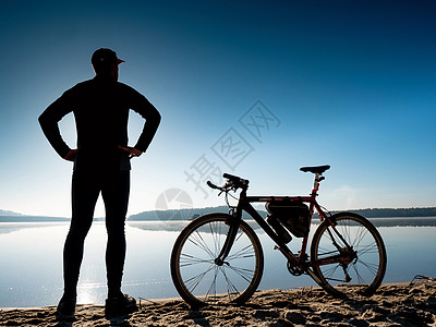 在海滩上骑自行车的车手 后视人 用碎石脚踏板站立着海岸车轮运输冒险轮子运动享受太阳乐趣眼镜图片