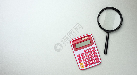 灰色背景 预算规划 利润计数的黑色塑料放大镜和粉红色计算器图片