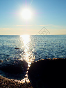 浪漫的海洋 泥沙从光滑的海中流出阴霾石头海岸岩石辉光地平线阳光紫色卵石天空图片