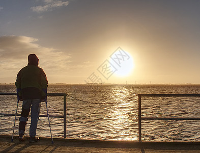 人徒步旅行者独自站立 观看海桥上日出日落男人海岸线长椅镜子橙子地平线远足者海洋思考图片