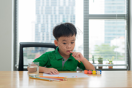 孩子们在学习桌上思考 孩子拿着笔和笔记本与思考的面部动作 男孩在学习桌上做作业与思考行为白色男生创造力桌子教育写作家庭作业学生微图片